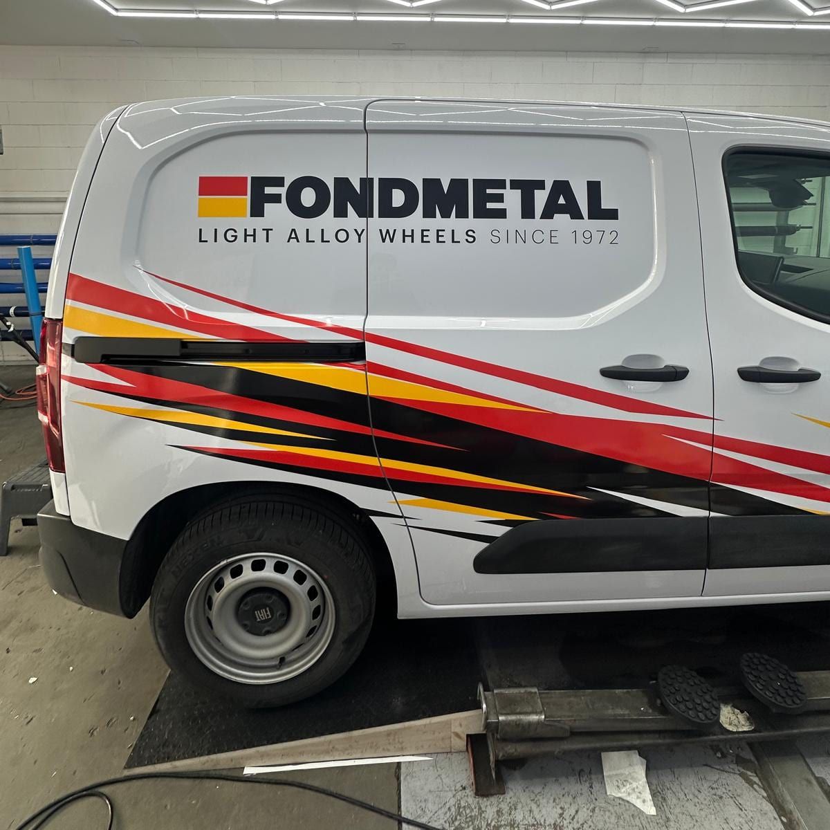 Furgone bianco Fondmetal con logo e fascia grafica rossa, gialla e nera sulla fiancata