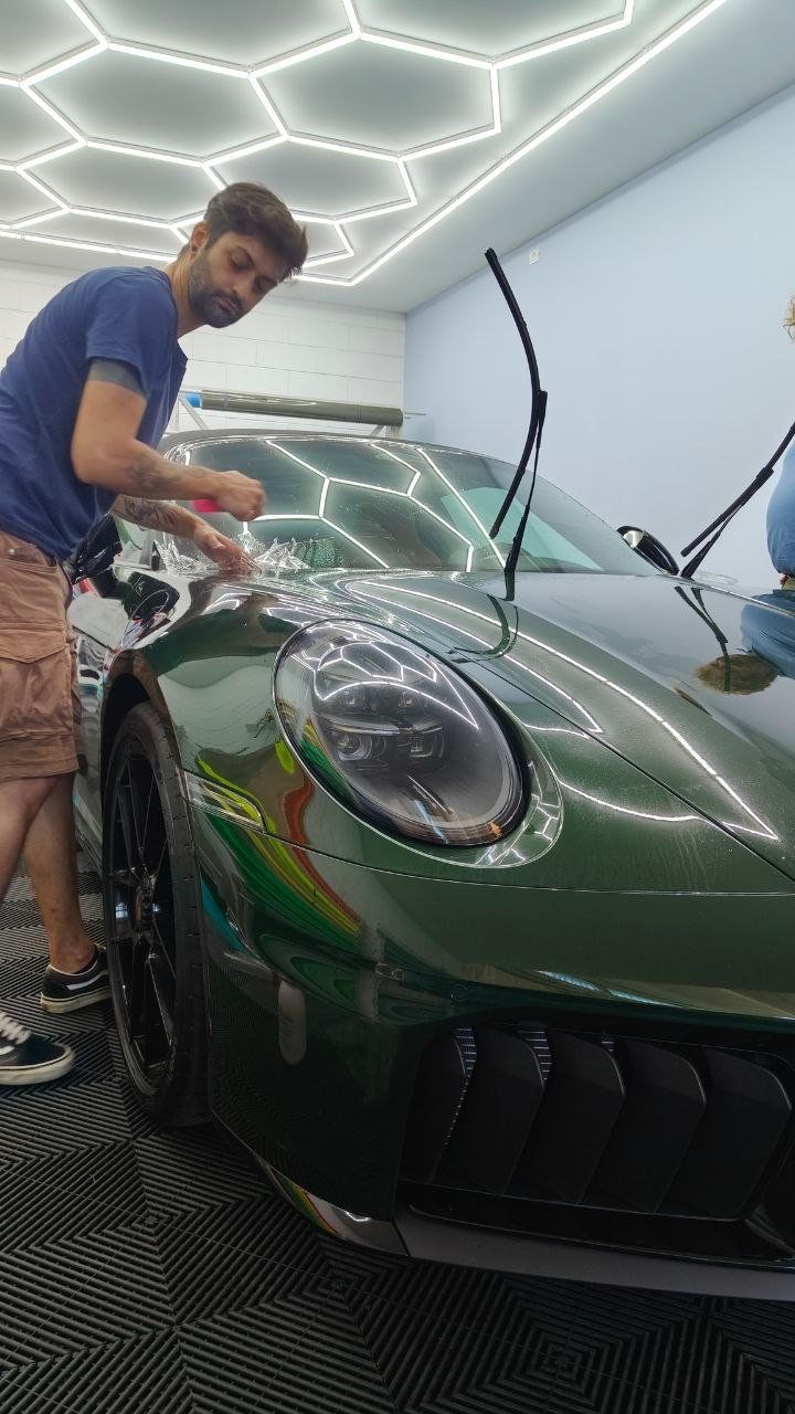 Tecnico applica pellicola protettiva PPF sul cofano di una Porsche 911 verde